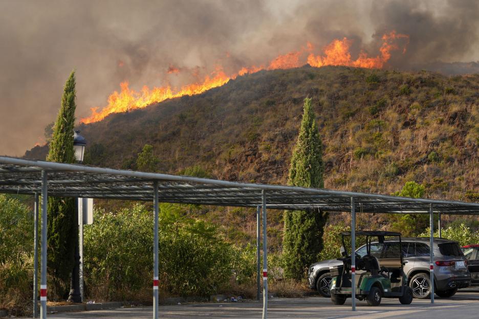 Wildfire burning across a mountainside in Estepona, Spain, with smoke filling the sky above.
