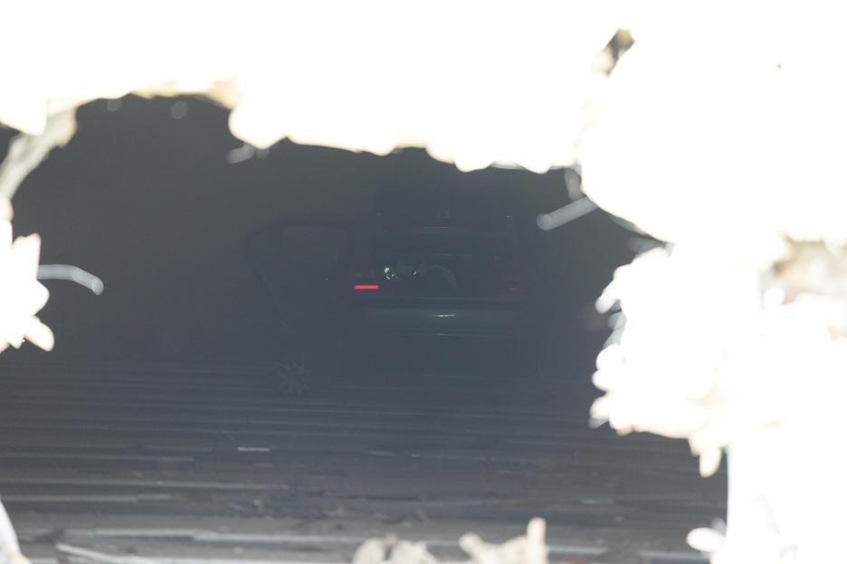 A dark car with a single red taillight is visible through a hole in a wall, positioned across multiple lanes of a bowling alley.