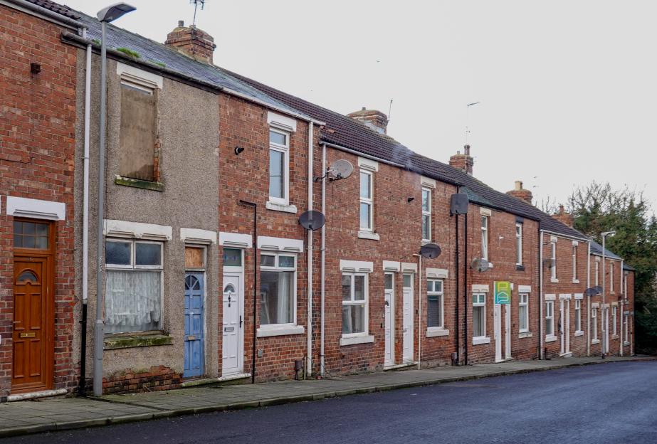 A street of brick terraced houses in Shildon Town, some with boarded-up windows and satellite dishes.