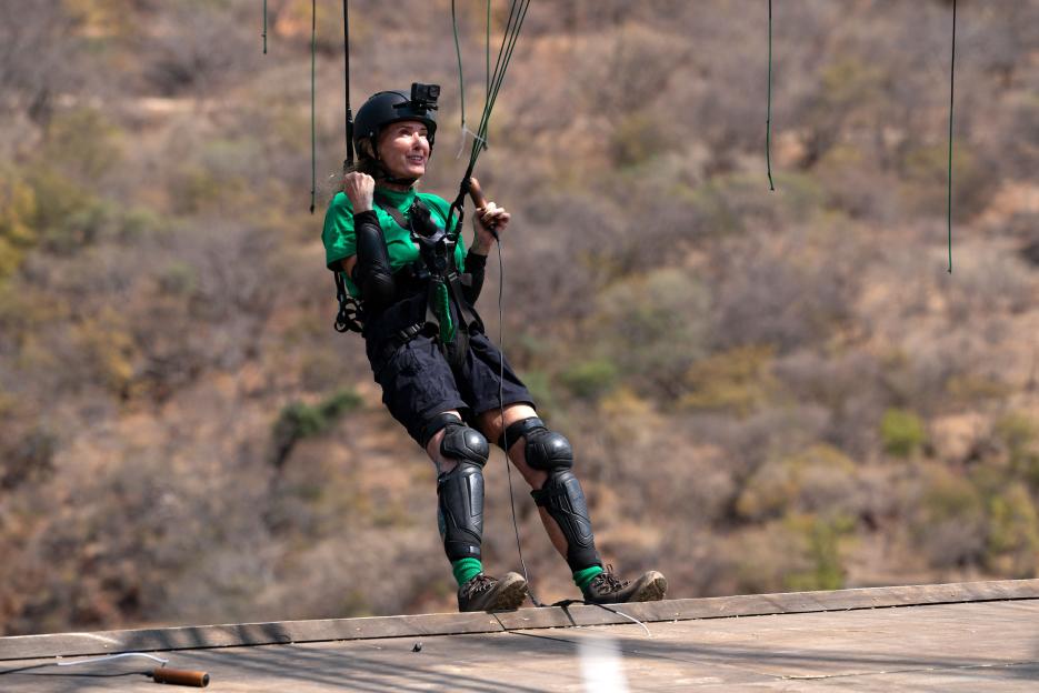 Beverley Callard wearing safety gear while suspended in the air during "Cut Throat Cliff" in "I'm A Celebrity... Get Me Out Of Here! South Africa"