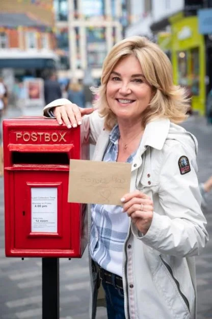 Anthea Turner holding an envelope addressed to "Future You" next to a red postbox.