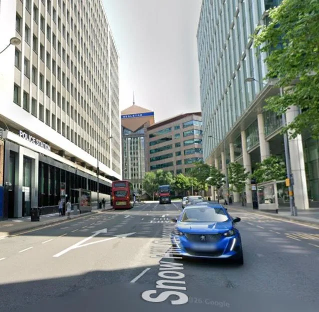 Street view of Snow Hill in Birmingham, featuring a blue car driving down the road with modern office buildings on both sides.