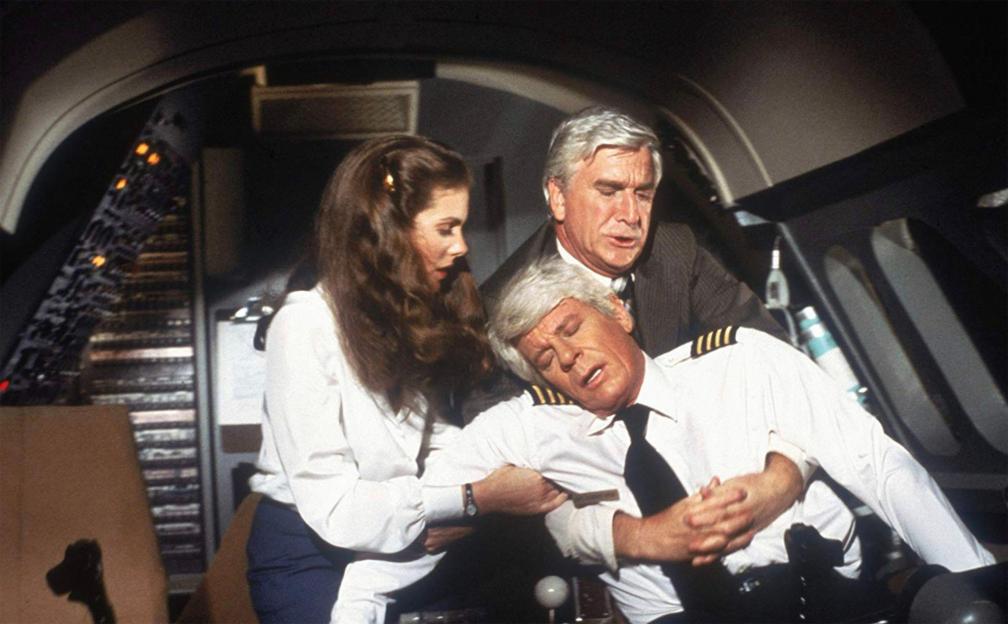 Julie Hagerty and Leslie Nielsen holding up an unconscious Peter Graves in the cockpit from the film Airplane!