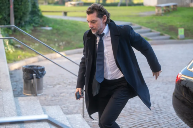 A man in a black coat and tie walking down steps while looking at his phone.
