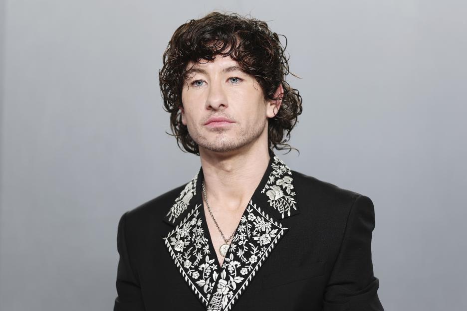 Barry Keoghan wearing a black suit with embroidered white lapels and a silver necklace.
