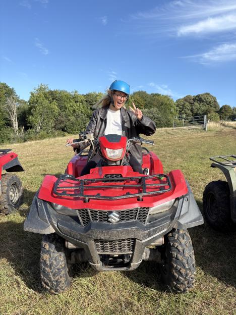 A woman in a blue helmet and black leather jacket smiles and gives a peace sign while sitting on a red ATV.