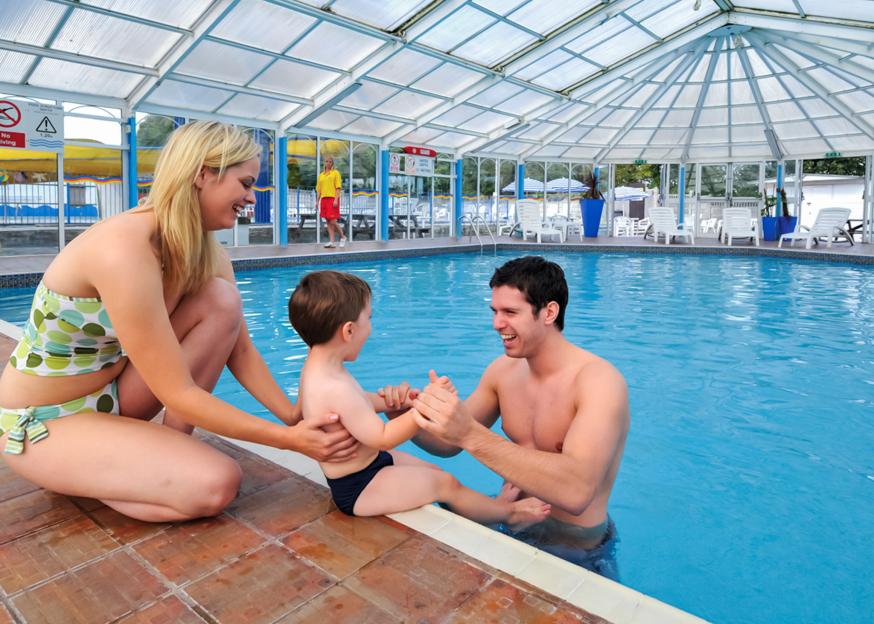 Family with young child playing in a swimming pool at Trelawne Manor Holiday Park in Cornwall.