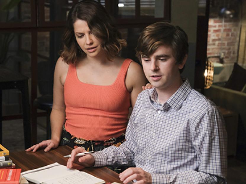 Two doctors, a man and a woman, leaning over a desk with a notebook.