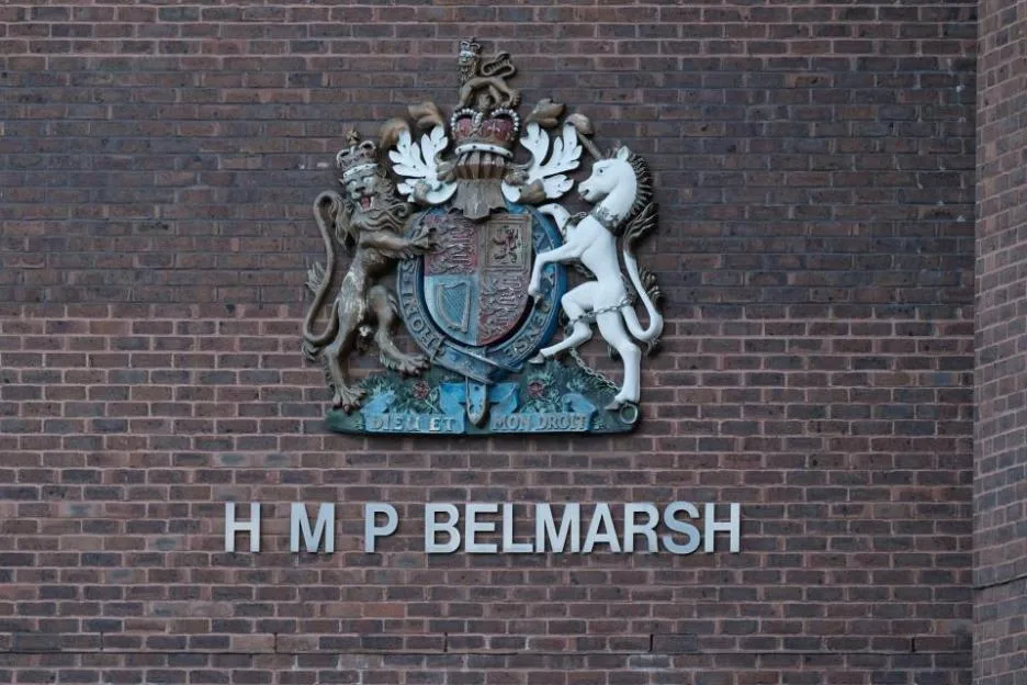 The exterior sign of HMP Belmarsh, featuring the Royal coat of arms above the prison's name mounted on a brick wall.
