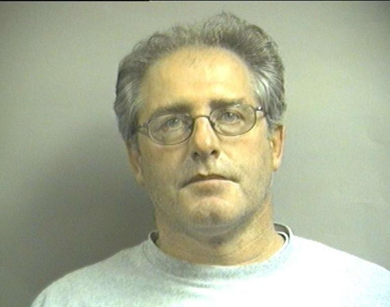 Mugshot of a middle-aged man with gray hair and glasses wearing a light-colored crewneck shirt.