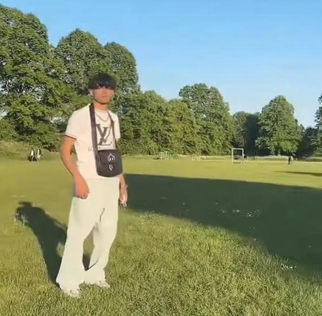 A man in a white t-shirt and light-colored pants stands on a grassy field.