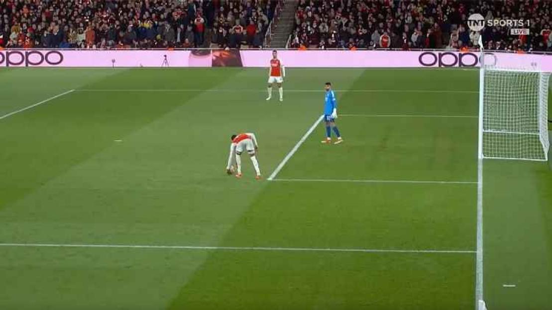 A football player in white and red bending over to place the ball for a corner kick.