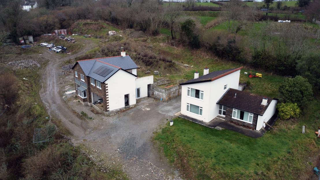 Aerial view of a new-build housing estate with two homes, one complete, and the other still under construction, on a steep, unpaved road.