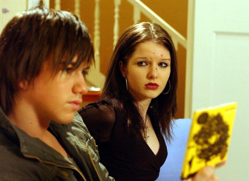 Rosie Webster (Helen Flanagan) looking disapprovingly at Craig Harris (Richard Fleeshman) who is holding a yellow book.