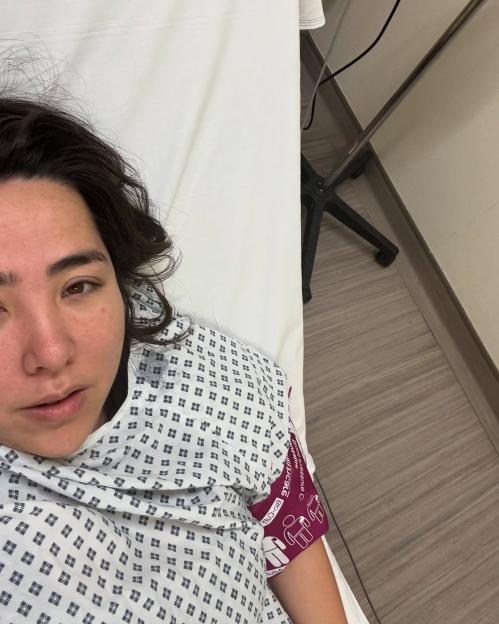 Michelle Elman lying in a hospital bed wearing a patient gown.