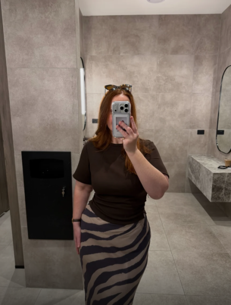 A woman in a ruched t-shirt and zebra-print skirt takes a mirror selfie.