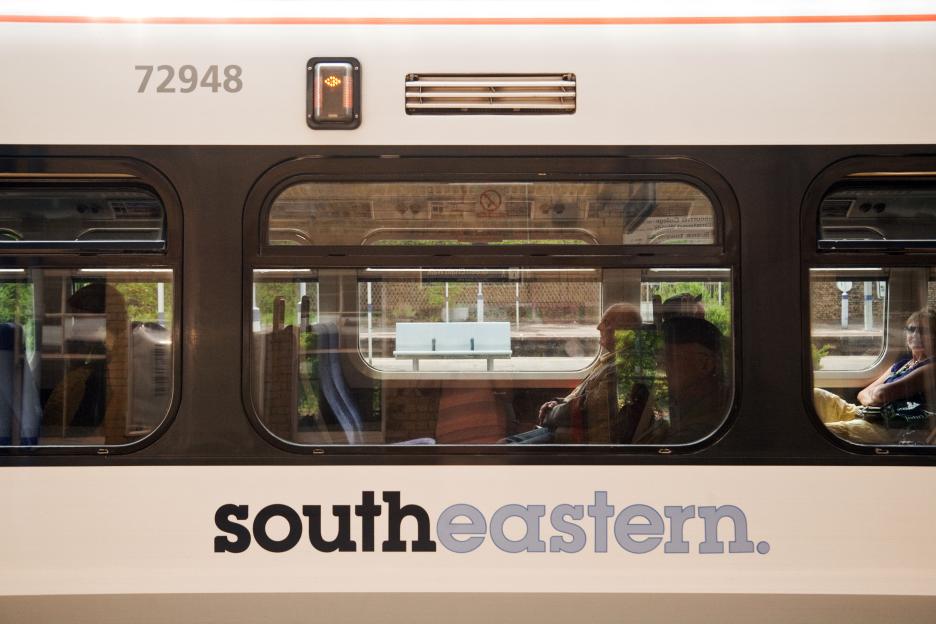 Side of a Southeastern train carriage, with a woman and a man visible through the windows.