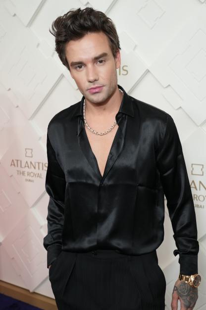 Liam Payne on the red carpet wearing an unbuttoned black satin shirt and a gold necklace.