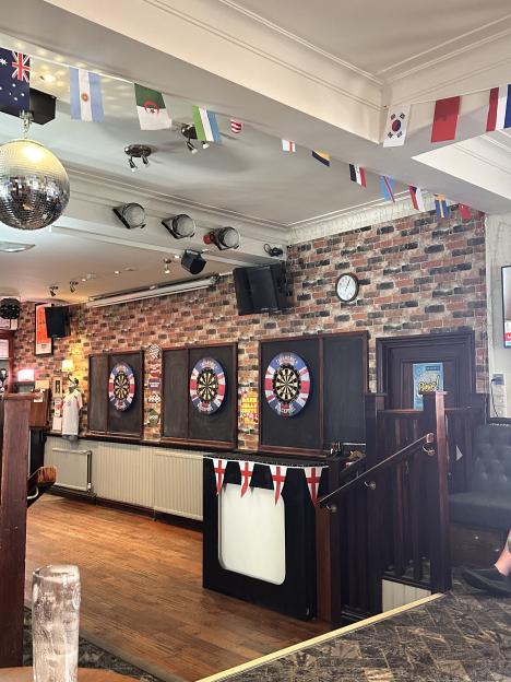 An interior shot of the Ardwick pub in Blackpool, with three dartboards on a brick wall, decorated with flags of various countries.