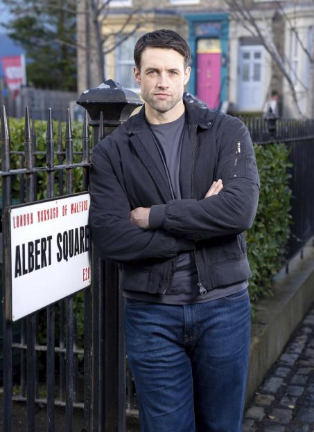 Mark Fowler Jr. (Stephen Aaron-Sipple) standing in front of an Albert Square street sign.