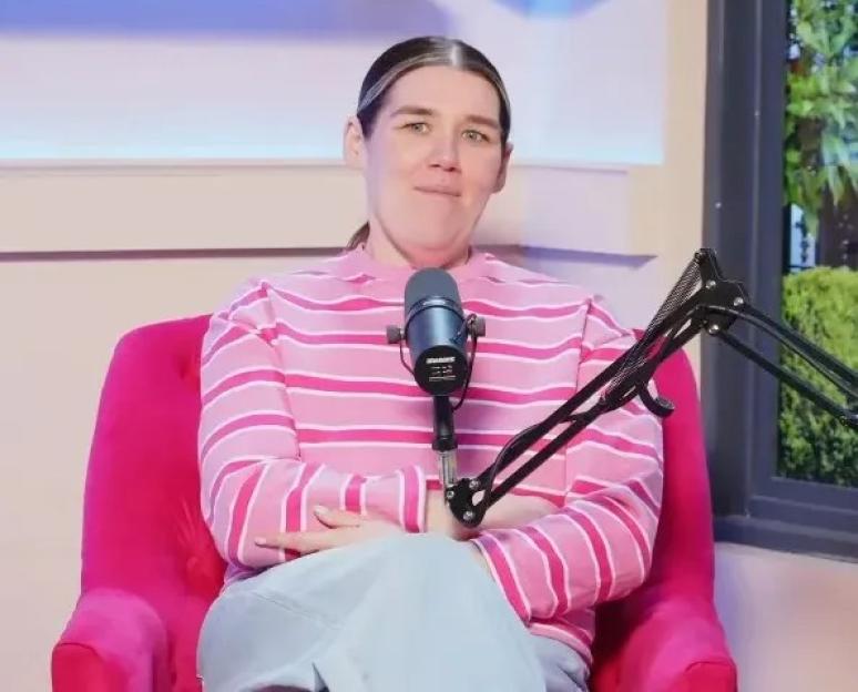 Woman in a pink striped shirt, seated in a pink armchair with a microphone in front of her.