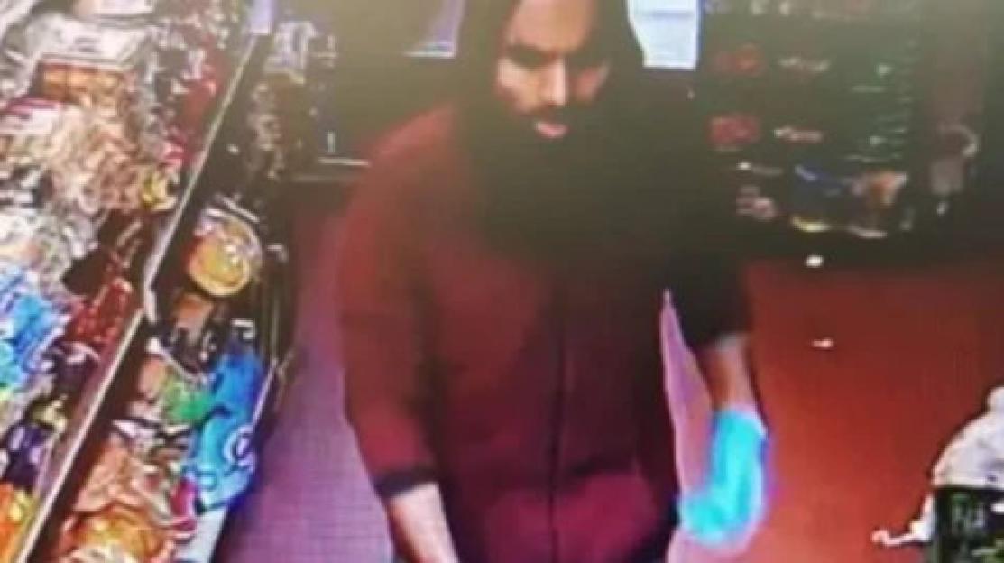 Ismail Ali in a red shirt with one light blue sleeve, captured by a security camera in a shop.