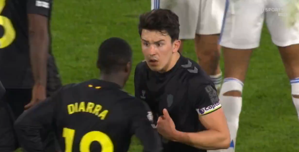 A soccer player wearing a captain's armband debates with another player.