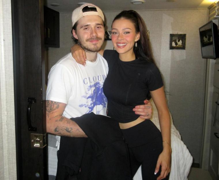 A man in a white T-shirt and a woman in a black outfit posing together.