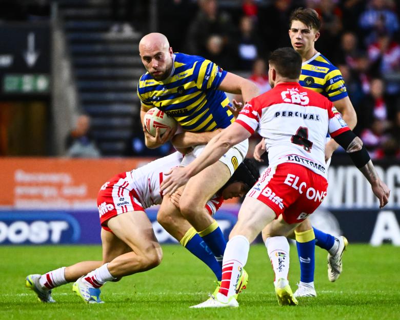 A rugby player in a yellow and blue striped jersey carrying the ball, being tackled by two players in white and red jerseys.