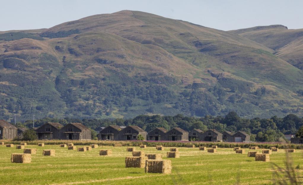 WW1 naval bomb depots and hay bales in a field with a mountain in the background.