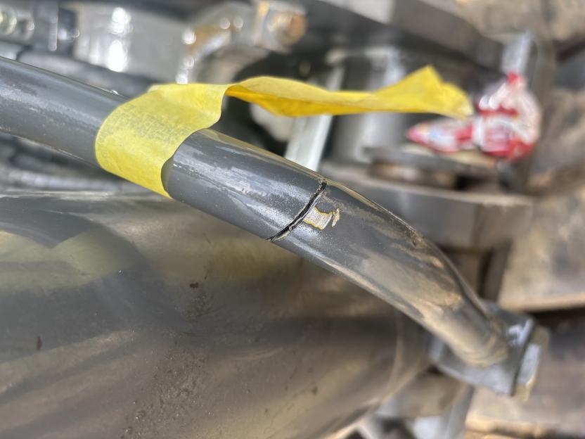 Damaged machinery with yellow tape partially covering a crack in a grey pipe.
