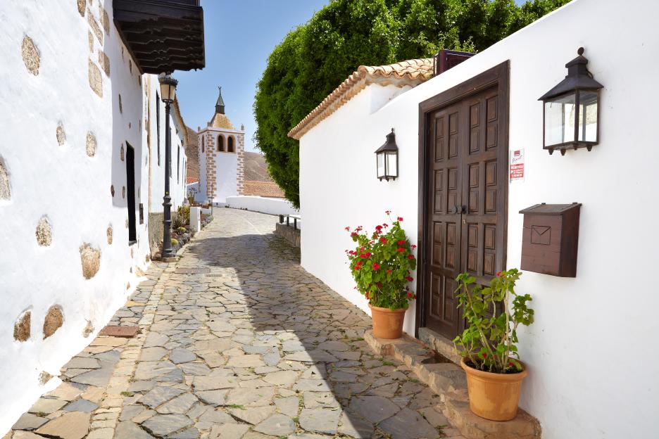 Cobbled street in Betancuria, Fuerteventura, with white buildings and a church tower.