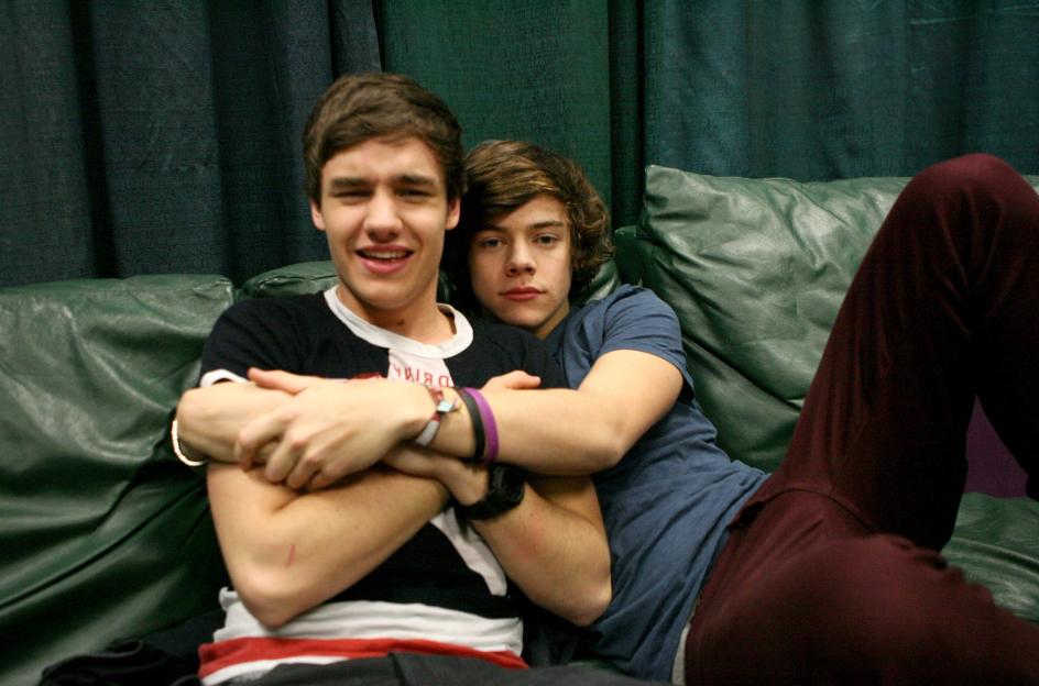 Liam Payne and Harry Styles of One Direction embrace on a green couch backstage.