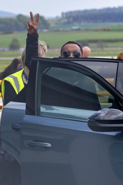 Amol Rajan, in sunglasses, peeking over a car door, and another person making a peace sign in the background.