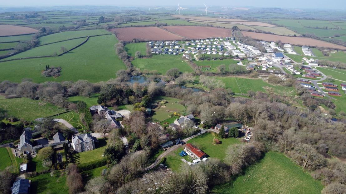 Aerial view of the Luney Barton hamlet in the foreground and the Meadow Lakes Holiday Park in the background, surrounded by green fields.