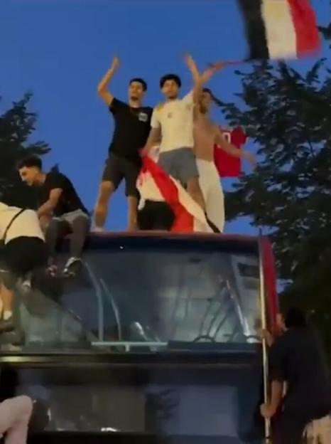 Egyptian fans celebrate by standing on top of a double-decker bus while holding flags.