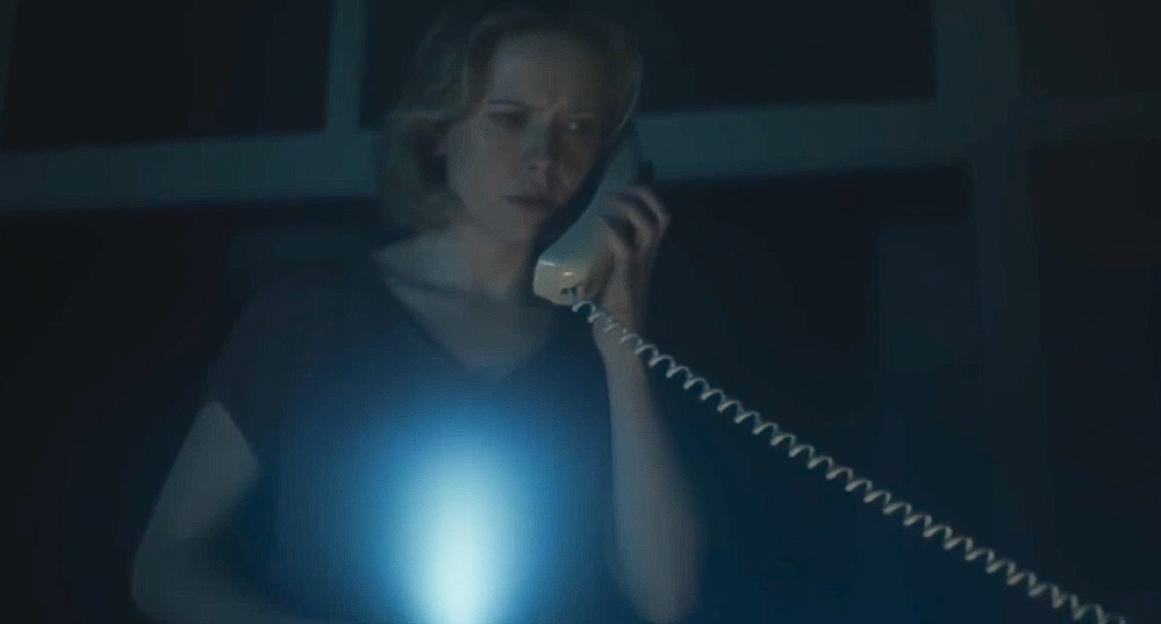 A woman with a worried expression holds a phone to her ear in a dark room, illuminated by a blue glow from below.