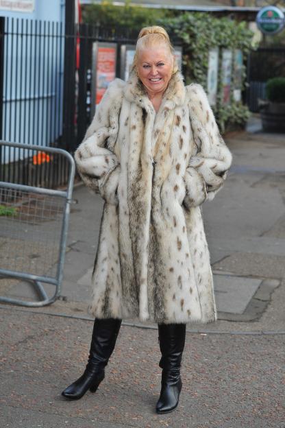 Celebrity Big Brother contestant Kim Woodburn smiles while wearing a white fur coat and black leather boots.