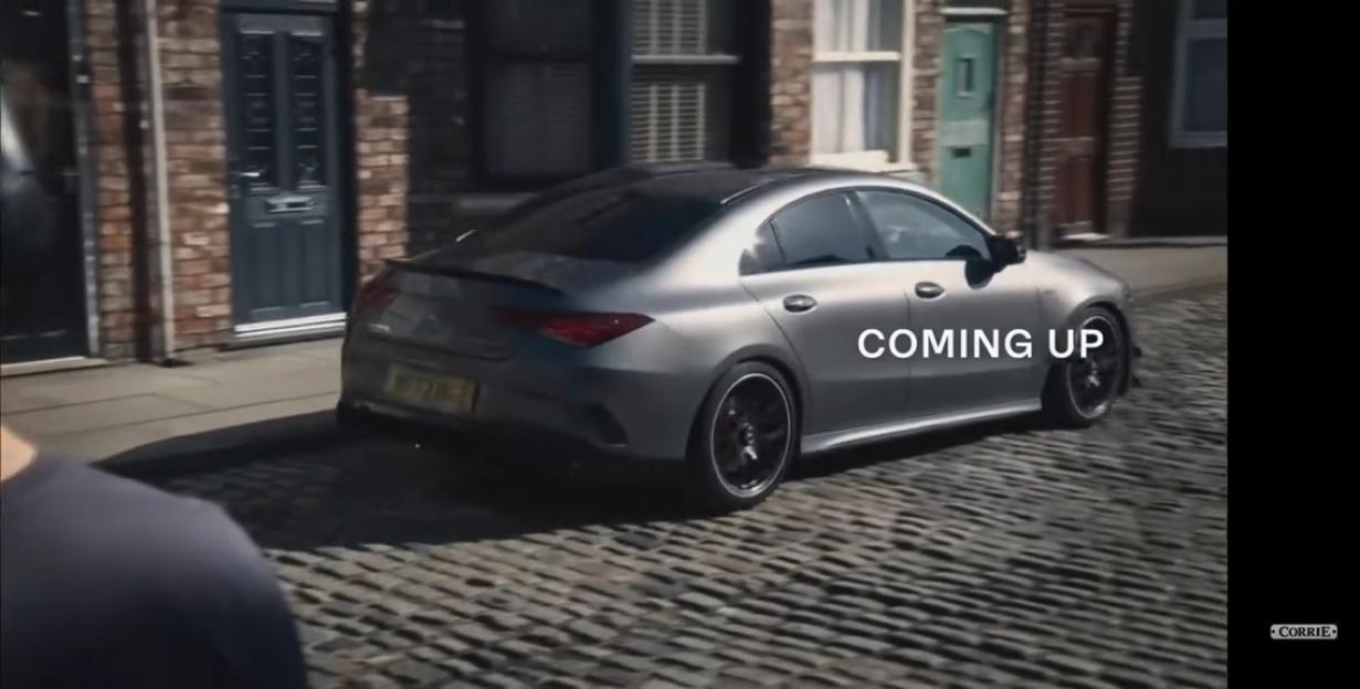 A gray car driving on a cobblestone street with the text "COMING UP" overlaid.