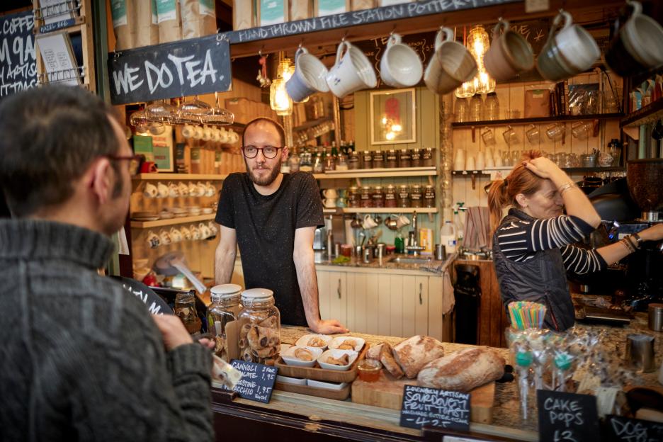 A barista serving a customer at Market House Coffee in Altrincham, with pastries and sourdough bread on display.