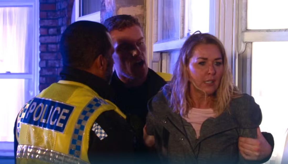A police officer with his back to the camera, a man with his mouth open, and a woman with light brown hair, being restrained.