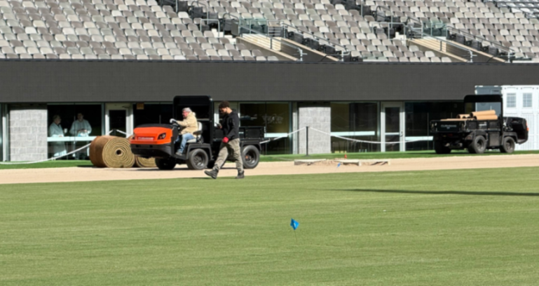Workers preparing a sports field with sod rolls and utility vehicles.