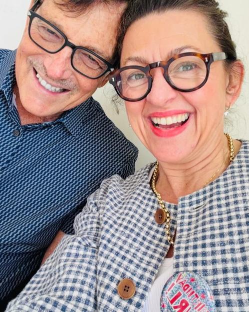 A man and a woman in glasses smile broadly at the camera.