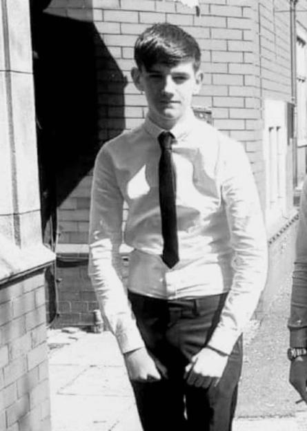 Black and white photo of a young man in a white shirt and black tie standing outside.