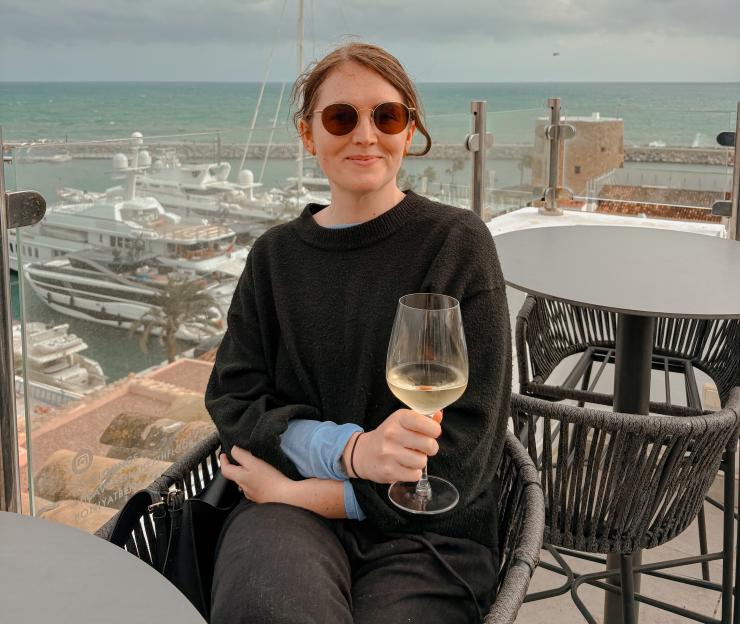 Woman in sunglasses on a balcony overlooking a marina, holding a glass of white wine.