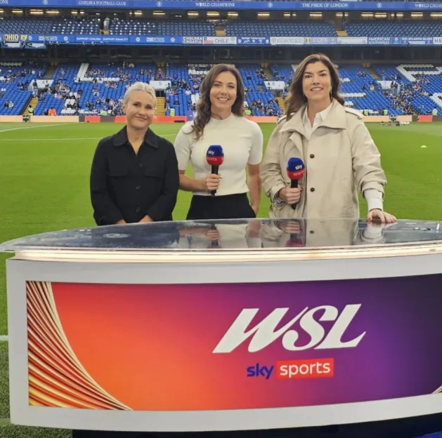 Rachel Corsie on Sky Sports broadcasting live from a football stadium alongside two colleagues behind a desk with the WSL Sky Sports logo.