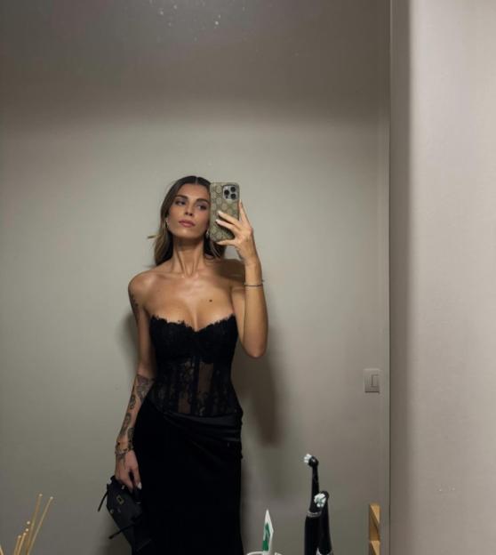 A woman in a black lace bustier and skirt taking a mirror selfie.