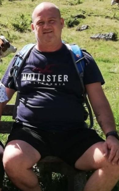 A man in a navy blue Hollister t-shirt and black shorts sits on a bench in a field.