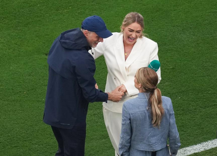 Two women and one man, standing on a green field, talking.