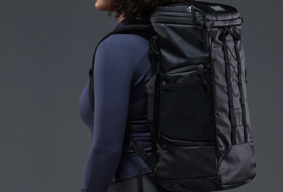 Side profile of a woman with curly hair wearing a long-sleeved navy top and a black backpack.